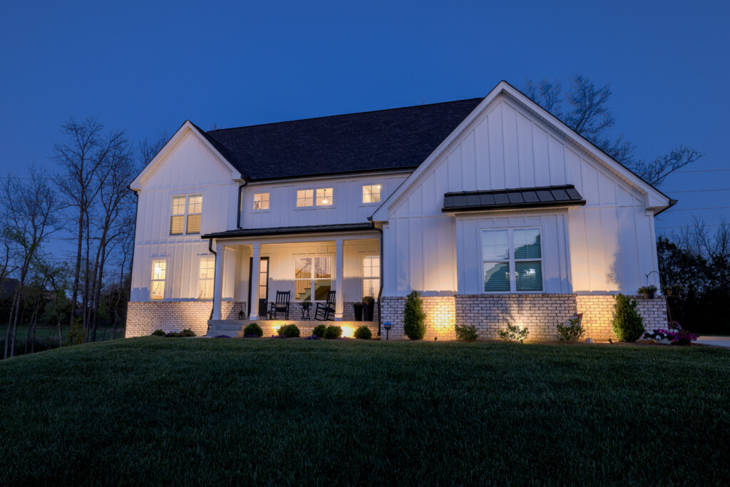 Stunning twilight image of a modern two-story farmhouse-style home with glowing interior lights, a well-manicured lawn, and soft outdoor lighting that highlights the architectural details against a clear evening sky.
